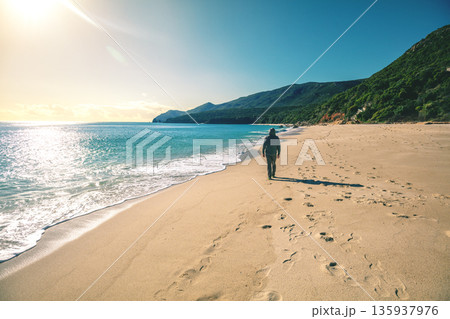 Seascape on a sunny day. A human walks on the beach. Galapinhos beach on a sunny day. Rocky seascape. Setubal region, Atlantic Ocean, Portugal 135937976