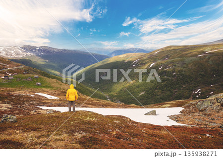 View from Mount Hoven to the picturesque valley and lake Lovatnet on a cloudy day. A man looks at the breathtaking view. Loen, Norway. View from Mount Hoven to the picturesque valley and lake Lovatnet on a cloudy day. A man looks at the breathtaking view. Loen, Norway. 135938271