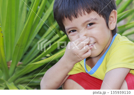 Portrait of Asian little boy squeeze the nose against of green plant background 135939110