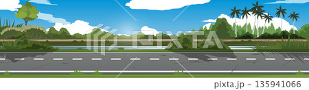 Horizontal of a scenic asphalt road passing through a lush green countryside. Landscape features a variety of trees tropical palms and dense bushes under blue sky with soft white clouds. 135941066