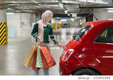 A woman wearing a hijab opens the trunk of her car after a shopping trip in a parking garage 135941899