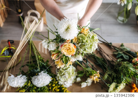 Florist arranges fresh blossoms on paper covered table in bright studio. Artisan craftsmanship, small business growth, floral design. 135942306