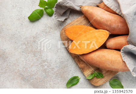 Sweet potatoes on cutting board with basil leaves 135942570