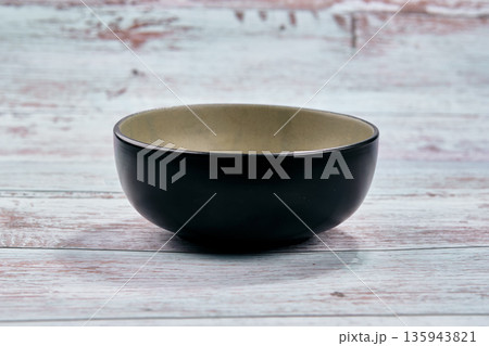 Dark-hued stoneware vessel reveals a luminous light-colored core, resting on a textured, pale wooden table 135943821