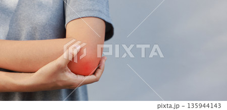 Close-up of woman hand holding painful injured elbow with red inflamed spot. Concept of joint bone pain, muscle injury, arthritis, tendonitis, or ache from sports or work in outdoor background. Close-up of woman hand holding painful injured elbow with red inflamed spot. Concept of joint bone pain, muscle injury, arthritis, tendonitis, or ache from sports or work in outdoor background. 135944143