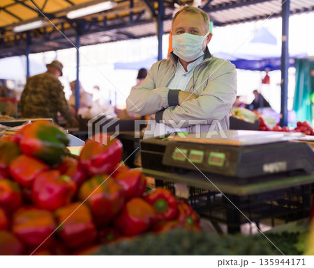 Man in face mask purchasing pepper in greengrocery Man in face mask purchasing pepper in greengrocery 135944171