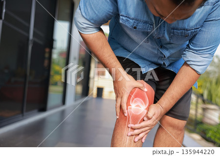 Close-up of hand holding painful injured knee with red inflamed spot and X-ray bone skeleton joint overlay. Medical concept of fracture, arthritis, tendonitis, or muscle ache in outdoor background. Close-up of hand holding painful injured knee with red inflamed spot and X-ray bone skeleton joint overlay. Medical concept of fracture, arthritis, tendonitis, or muscle ache in outdoor background. 135944220