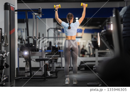 Woman training shoulders with dumbbells in fitness gym Woman training shoulders with dumbbells in fitness gym 135946305