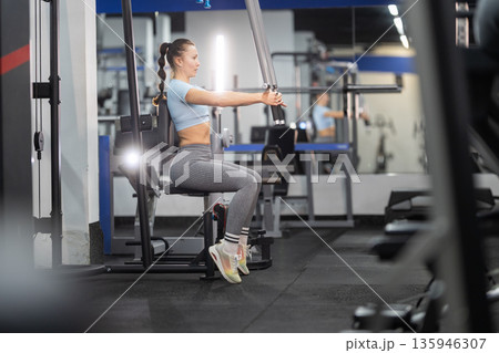 Woman exercising on chest press machine in gym Woman exercising on chest press machine in gym 135946307
