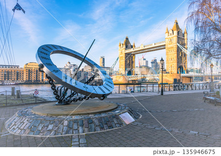 A large sundial stands prominently by the River Thames near Tower Bridge. The sun casts a shadow, showcasing the unique design against the backdrop of iconic London architecture. 135946675