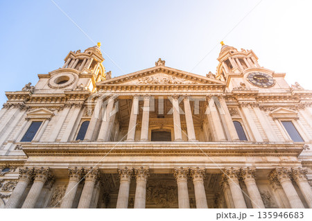 St. Pauls Cathedral stands tall in London. Visitors gather around the front portal. The sun shines on the historic building, highlighting its impressive architecture. 135946683
