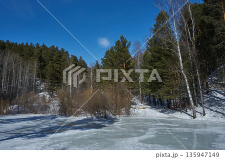 Frozen lake with forest on the shore. Winter landscape with snow forest lake and blue sky perfect for nature travel and climate articles. 135947149