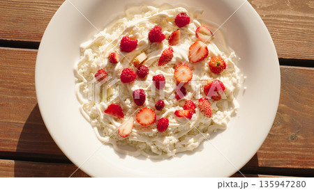Top View Cottage Cheese With Sour Cream, Fresh Strawberries, and Raspberries Served on a White Plate, and Wooden Table, Presented in Natural Sunlight for a Healthy Breakfast or Dessert. Top View Cottage Cheese With Sour Cream, Fresh Strawberries, and Raspberries Served on a White Plate, and Wooden Table, Presented in Natural Sunlight for a Healthy Breakfast or Dessert. 135947280