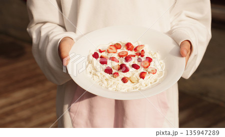 White plate with cottage cheese, strawberries, and raspberries in hands girl, ready to eat on a sunny day. 135947289