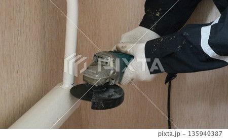 A worker cuts a pipe leading to the regulator using an angle grinder; an old cast-iron heating system painted white; dismantling of water pipes using an angle grinder in a room undergoing renovation. A worker cuts a pipe leading to the regulator using an angle grinder; an old cast-iron heating system painted white; dismantling of water pipes using an angle grinder in a room undergoing renovation. 135949387