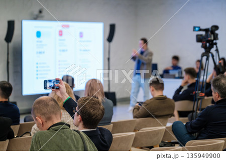 Engaging business conference with a speaker presenting to attentive audience as cameras record Engaging business conference with a speaker presenting to attentive audience as cameras record 135949900