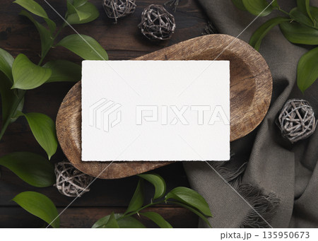 Horizontal card mockup on brown wooden tray near green leaves and grey fabric top view Horizontal card mockup on brown wooden tray near green leaves and grey fabric top view 135950673