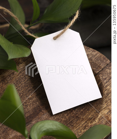 Vertical gift tag mockup on brown wooden tray near green leaves and grey fabric closeup Vertical gift tag mockup on brown wooden tray near green leaves and grey fabric closeup 135950675