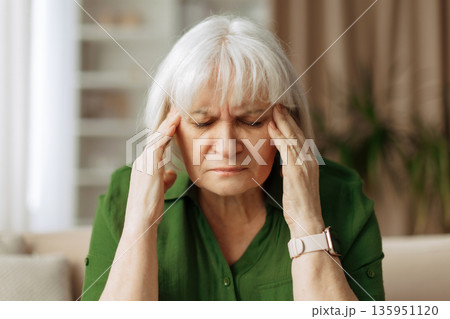 Senior caucasian woman touching temples with eyes closed at home, experiencing headache Senior caucasian woman touching temples with eyes closed at home, experiencing headache 135951120
