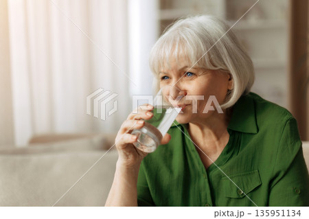 Senior woman drinking water at home, elderly female staying hydrated and healthy 135951134