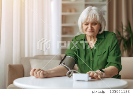 Elderly caucasian woman calmly measuring blood pressure at home 135951188