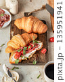 Croissant sandwich with salami, sausage, cherry tomatoes, soft cheese and chard micro greens on wooden board kitchen table background for savory healthy breakfast 135951941