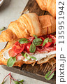 Croissant sandwich with salami, sausage, cherry tomatoes, soft cheese and chard micro greens on wooden board close up for savory healthy breakfast 135951942