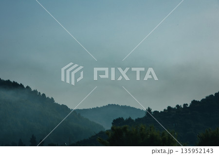 A sweeping mountain landscape in August 2025, with tiered, wooded hills under a clear summer sky. A sweeping mountain landscape in August 2025, with tiered, wooded hills under a clear summer sky. 135952143