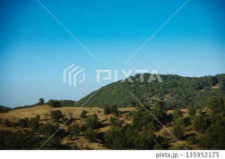 A sweeping mountain landscape in August 2025, with tiered, wooded hills under a clear summer sky. A sweeping mountain landscape in August 2025, with tiered, wooded hills under a clear summer sky. 135952175