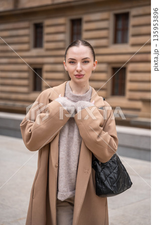 Portrait of young beautiful woman wearing coat walking in the city centre of Prague, Europe Portrait of young beautiful woman wearing coat walking in the city centre of Prague, Europe 135953896