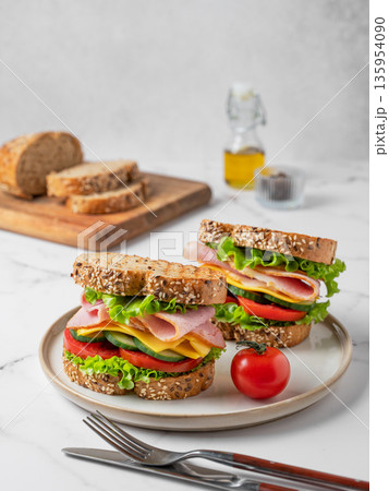 Two sandwiches with ham, cheese, lettuce, vegetables and seeded bread on a plate Two sandwiches with ham, cheese, lettuce, vegetables and seeded bread on a plate 135954090