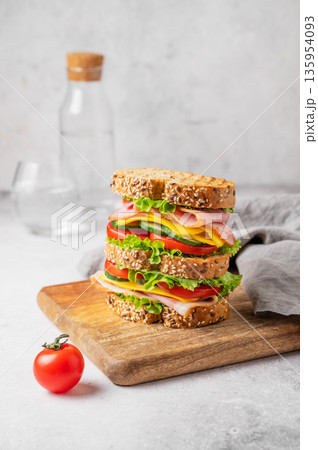 A triple sandwich with ham, cheese, lettuce, and vegetables on whole grain bread on a wooden board A triple sandwich with ham, cheese, lettuce, and vegetables on whole grain bread on a wooden board 135954093