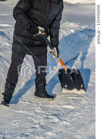A person in a black jacket shovels snow on a sunny day after a blizzard. A person in a black jacket shovels snow on a sunny day after a blizzard. 135956098