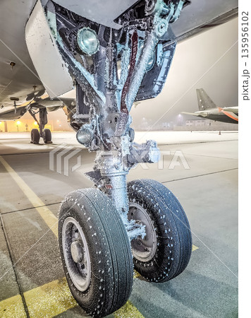 Icy landing gear of a passenger plane at a winter airport at night. Icy landing gear of a passenger plane at a winter airport at night. 135956102
