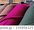 Close-up view of a row of colored womens wool coats hanging neatly on a rack in a store. 135956125