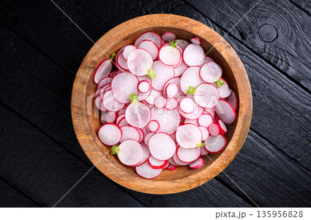Overhead view of radish slices in wooden bowl on black surface Overhead view of radish slices in wooden bowl on black surface 135956828