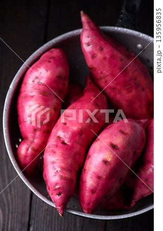 Raw sweet potatoes in metal colander on dark background 135956835