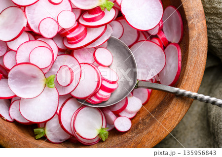 Sliced red radishes in wooden bowl with metal spoon Sliced red radishes in wooden bowl with metal spoon 135956843