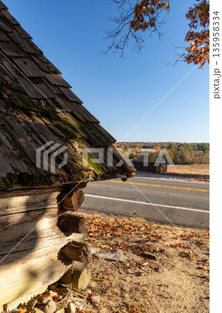 A log cabin with moss growing on it sits on a dirt road 135958334