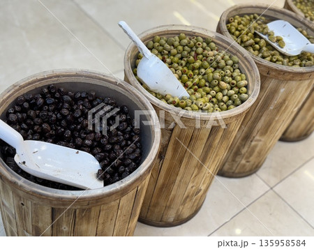 Barrels of green and black olives with scoops in wooden containers in a market setting Barrels of green and black olives with scoops in wooden containers in a market setting 135958584