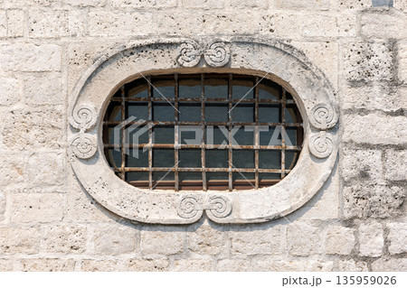 A rustic oval window set in a light stone wall 135959026