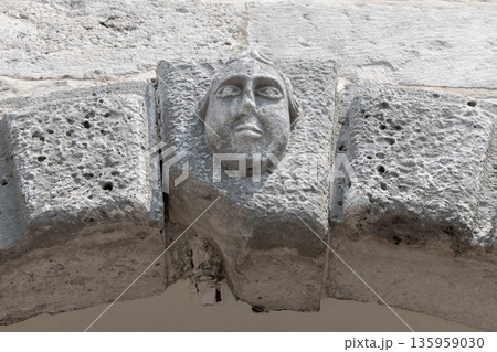 A weathered stone arch features a carved human face A weathered stone arch features a carved human face 135959030