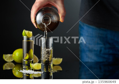 Tequila shots with salt and lime slices on a black reflective background. 135960649