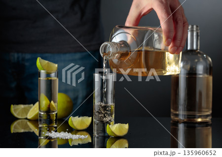 Tequila shots with salt and lime slices on a black reflective background. 135960652