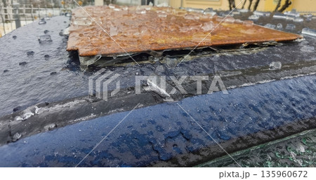Rusty metal sheet placed on icy car roof with frozen droplets and sheen under winter light, showing corroded surface texture against slick frozen background. 135960672