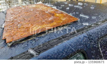 Rusted metal panel tilted on frozen car roof with melting ice and frost crystals reflecting cold winter conditions and textured corrosion over dull surface. Rusted metal panel tilted on frozen car roof with melting ice and frost crystals reflecting cold winter conditions and textured corrosion over dull surface. 135960673