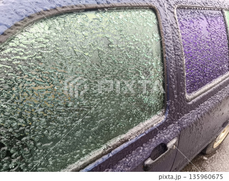 Close view of purple car side window encrusted with thick icy layer and frost glaze, showing opaque surface and winter condensation frozen in place. Close view of purple car side window encrusted with thick icy layer and frost glaze, showing opaque surface and winter condensation frozen in place. 135960675