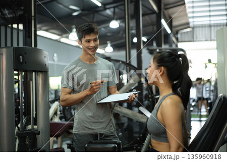 A woman is working out on an inner thigh machine while her trainer records the activity 135960918