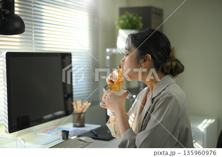 Businesswoman eating instant noodles at office desk, casual lunch break during workday in modern workspace. 135960976