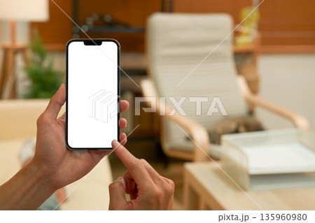 Close up view of a man using blank screen smartphone at living room 135960980